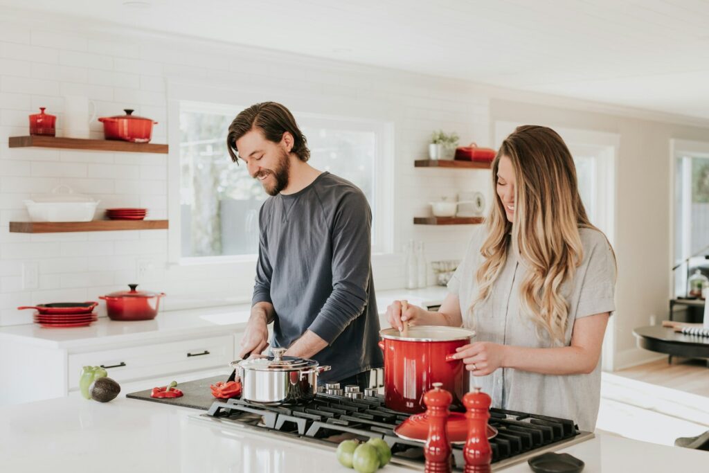 Bild eines jungen Paares beim Kochen in der Küche mit roten Töpfen und rotem Geschirr